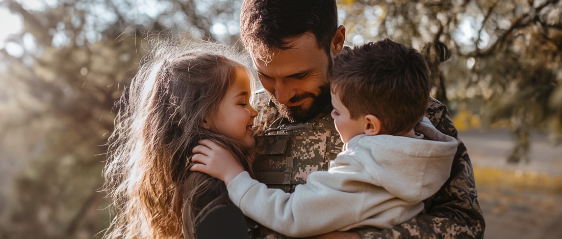 A soldier in uniform embraces his young son and daughter, mindful of how military life insurance protects them.