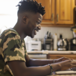 A young man dressed in soldier's camouflage happily uses a laptop with the eBenefits website on it.