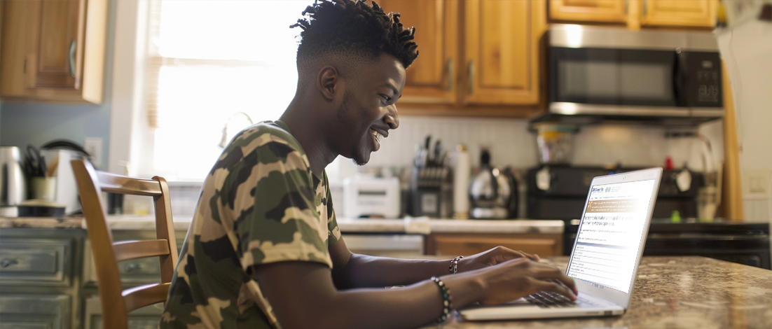 A young man dressed in soldier's camouflage happily uses a laptop with the eBenefits website on it.