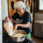 An elderly woman happily pours a bag of rice into a saucepan to make dinner.