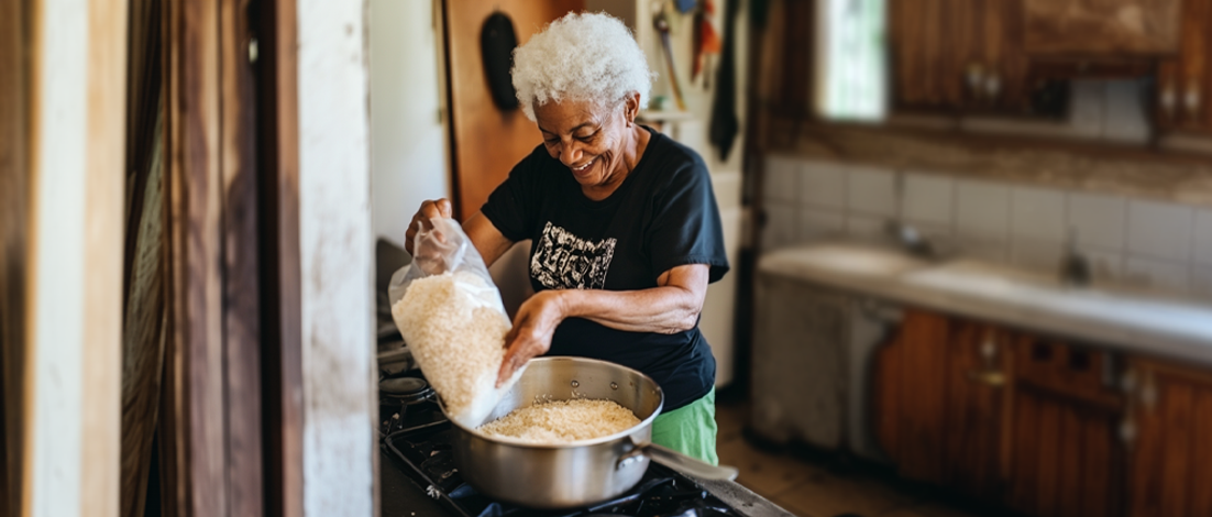 An elderly woman happily pours a bag of rice into a saucepan to make dinner.